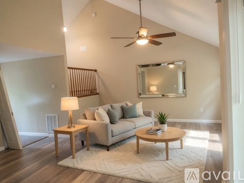 A living room with a grey couch, a wooden coffee table, a side table with a lamp, a ceiling fan, and a mirror on the wall.