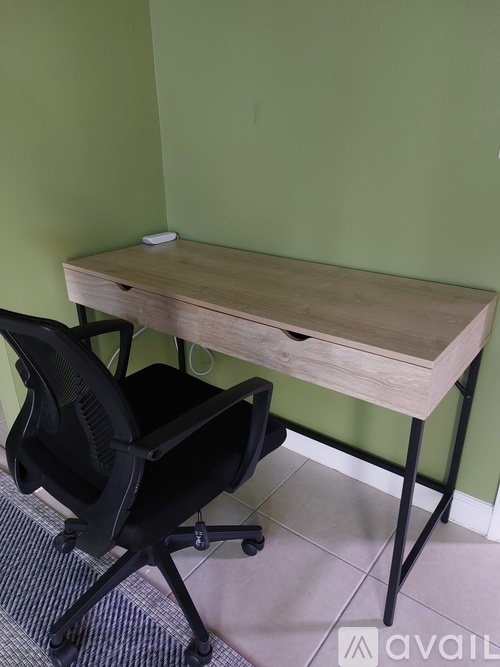 A black chair is in front of a green wall with a wooden desk.