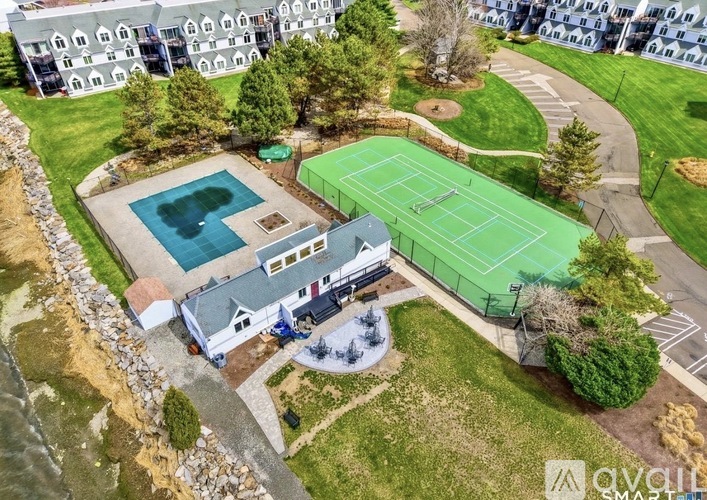 A tennis court is surrounded by a green fence and a swimming pool.