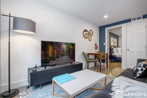 A living room with a grey sofa, a white coffee table, and a television on a cabinet.