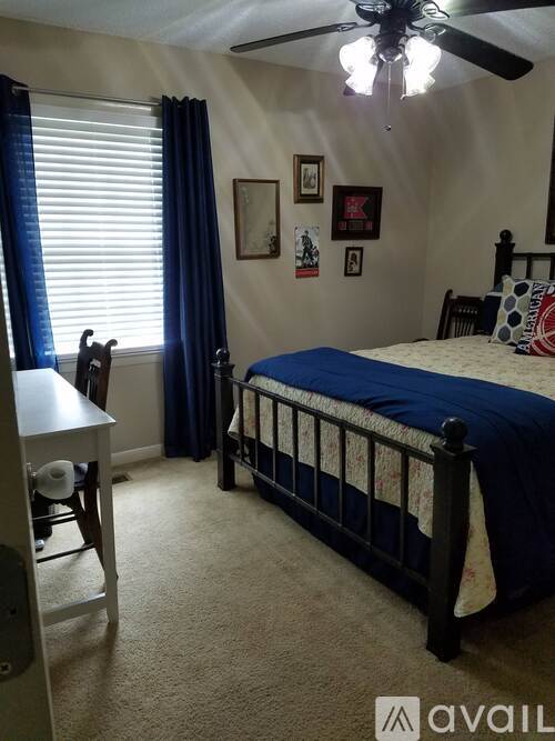 A bedroom with a bed, desk, chair, and ceiling fan.