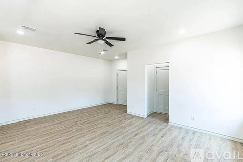 A spacious room with a ceiling fan and light fixture, and a wooden floor.