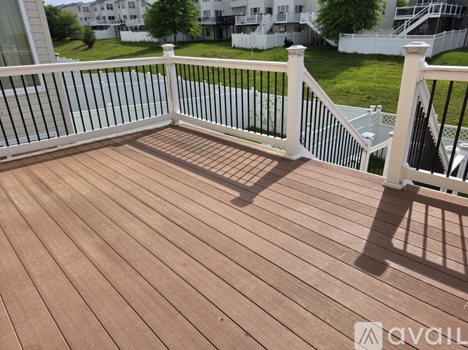 A wooden deck with a white railing and a view of a grassy area and buildings.
