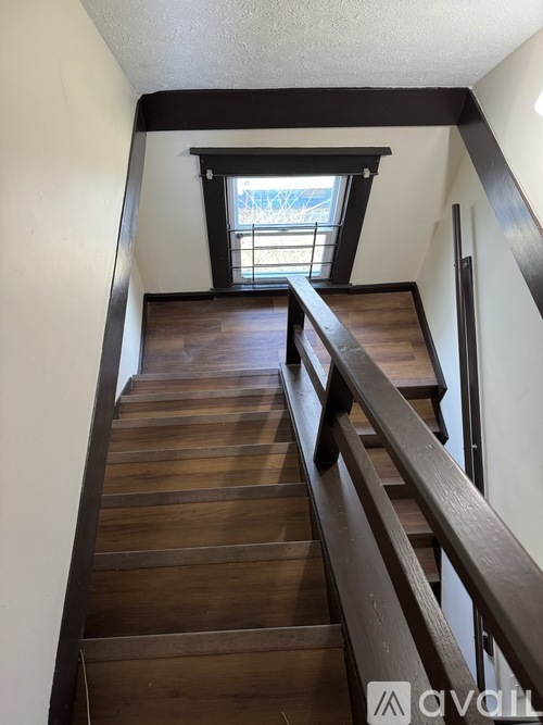 A wooden staircase with a metal railing leads up to a window.