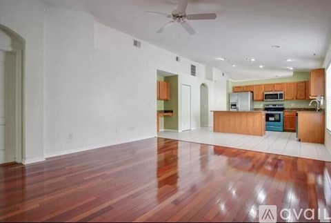 A spacious living room with hardwood floors and a kitchen area in the background.