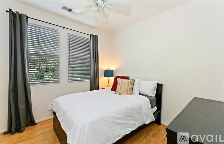 A bedroom with a bed, a ceiling fan, and a window with curtains.