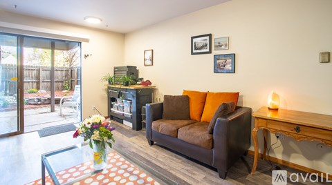 A living room with a brown couch and a glass coffee table with flowers in a vase.