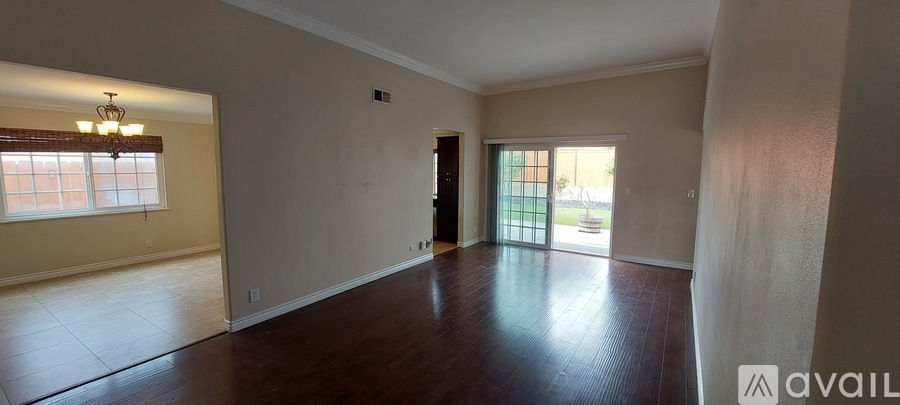 A spacious room with wooden floors and a sliding glass door leading to a balcony.