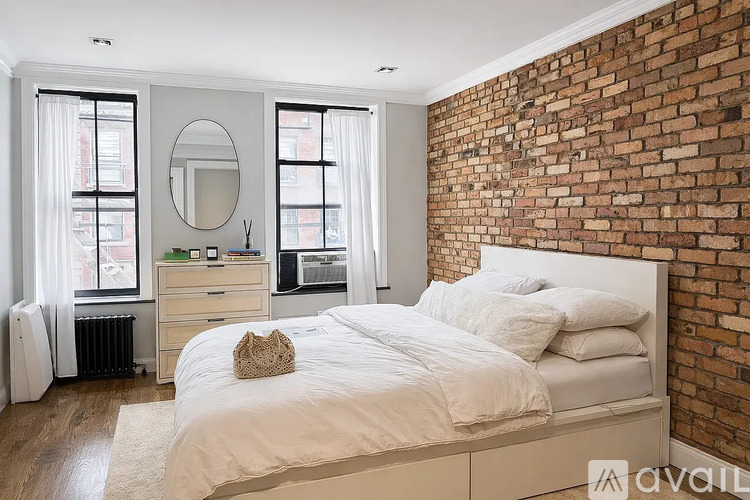 A bedroom with a white bed and a brick wall.