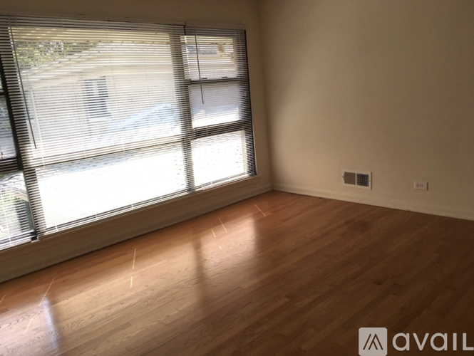A room with wooden flooring and a large window with blinds.