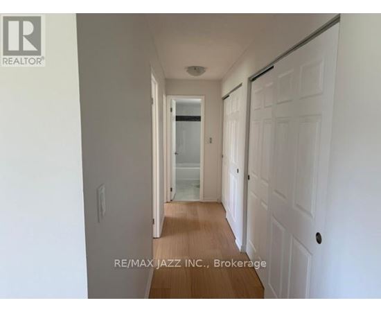A hallway with white walls and wooden floors leading to a door.