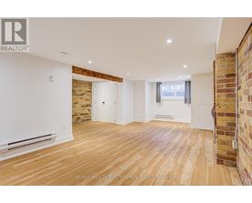 A spacious room with wooden flooring and a brick wall on one side.