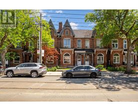 Two cars are parked on the side of a street in front of a large brick building.