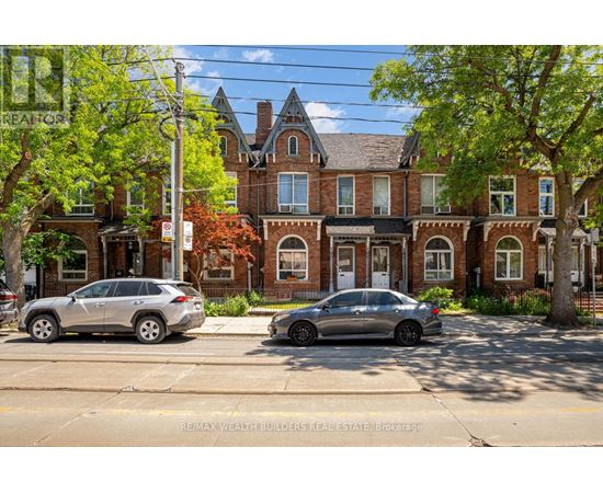 Two cars are parked on the side of a street in front of a large brick building.