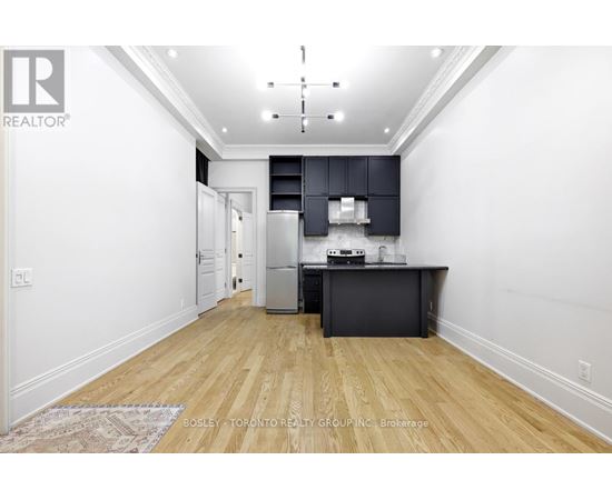 A kitchen with a refrigerator, oven, and microwave in a white room with wooden floors.