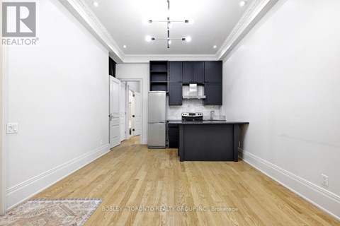 A kitchen with a refrigerator, oven, and microwave in a white room with wooden floors.