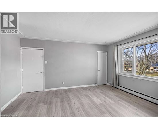 A room with a white door, a window with a view of trees, and a wooden floor.