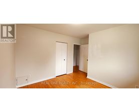A white room with wood floors and a Realty logo.