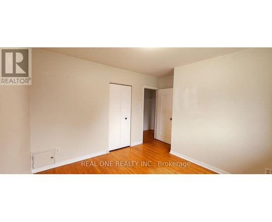A white room with wood floors and a Realty logo.