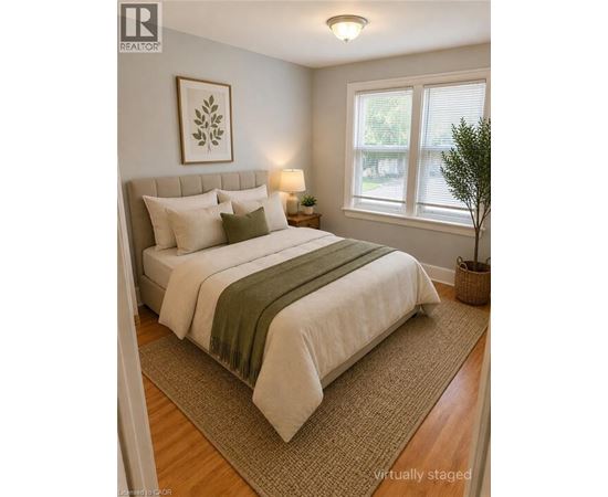 A bedroom with a bed, pillows, a lamp, a plant, and a framed picture on the wall.