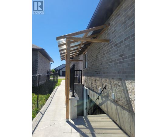 A wooden pergola attached to a brick wall with a concrete staircase leading up to it.