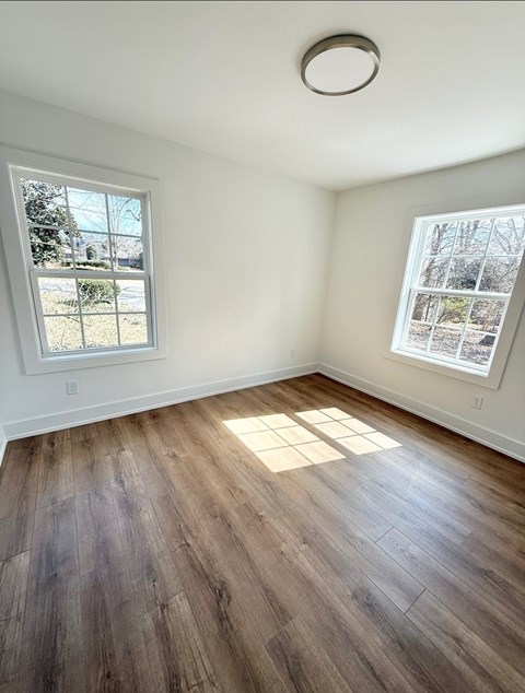 A room with wooden flooring and two windows.