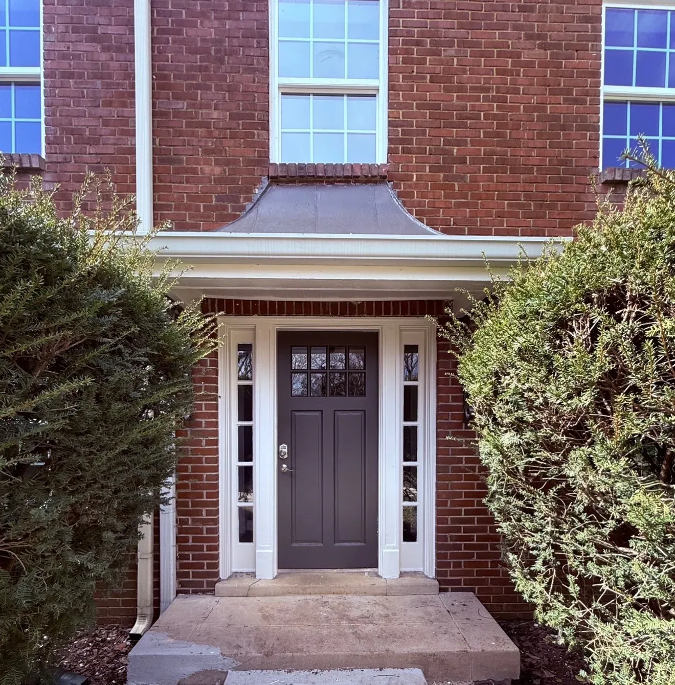 A brick house with a dark brown door and a small porch.