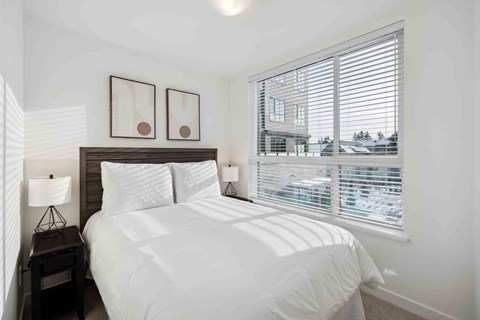 A bedroom with a large bed and a window with blinds.