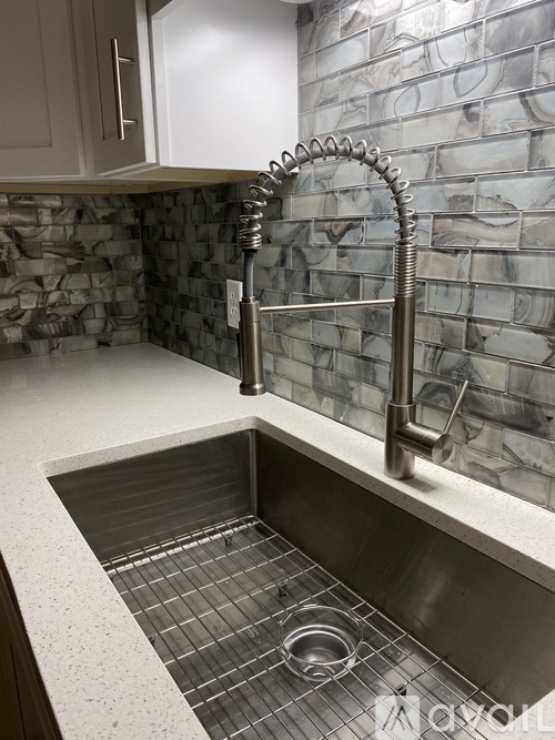 A kitchen sink with a silver faucet and a stone wall behind it.