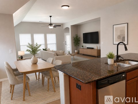 A kitchen with a dining table and chairs in the foreground and a living room with a couch and television in the background.