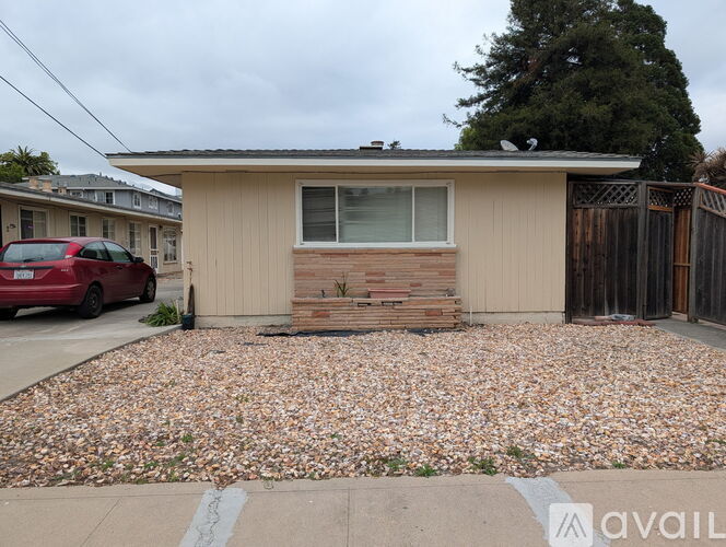 A house with a gravel driveway and a red car parked in front.