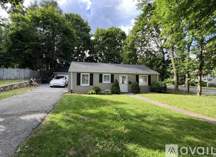 A house with a car parked in front and trees in the background.