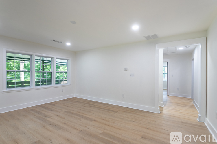 A spacious room with wooden flooring and a window with blinds.