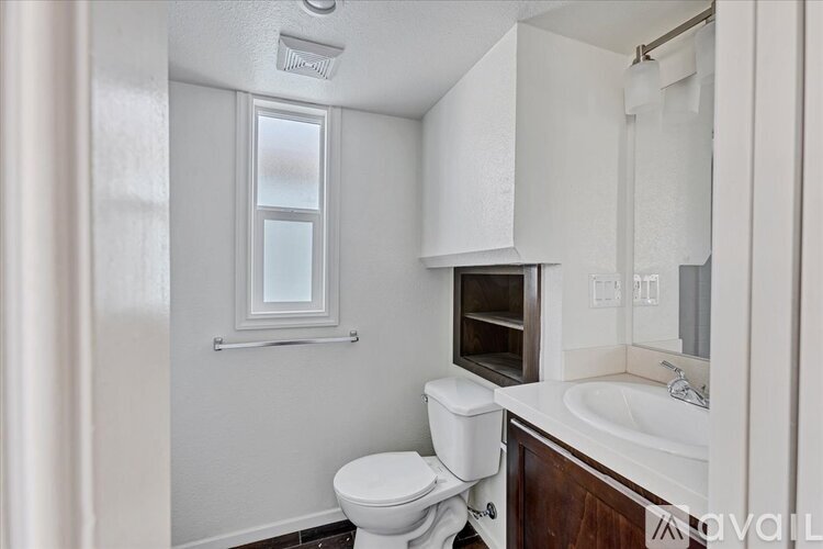 A white toilet sits in a small bathroom with a window above it.