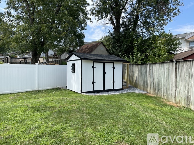 A small white shed with a black roof is situated in a grassy backyard.