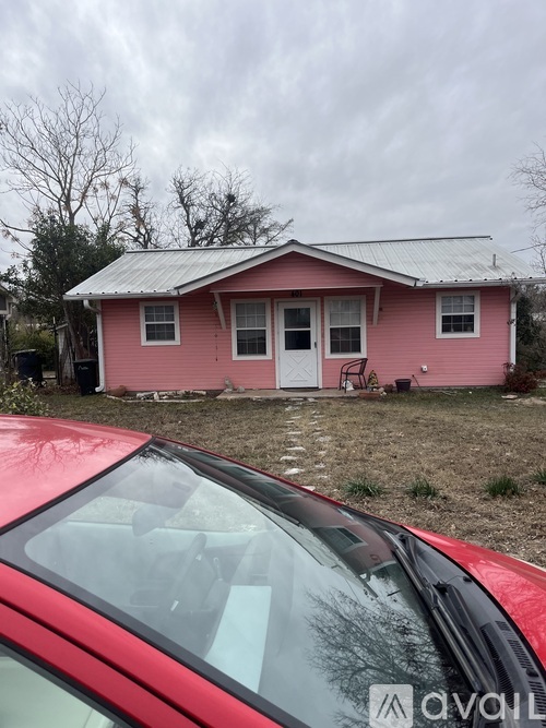A red car is parked in front of a pink house.