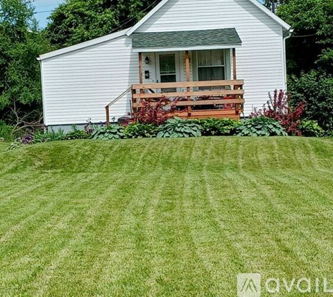 A white house with a wooden deck and green lawn.