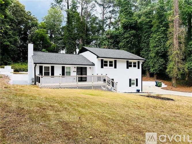 A white house with a black roof is surrounded by greenery.