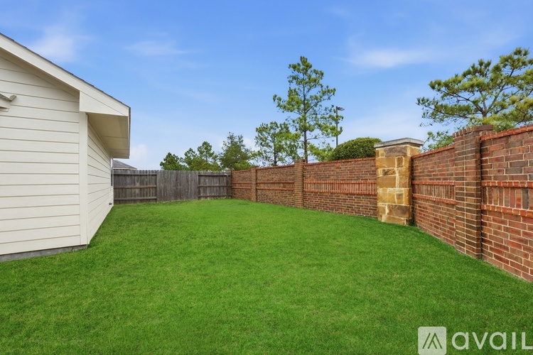 A backyard with a white house, green grass, and a brick wall.