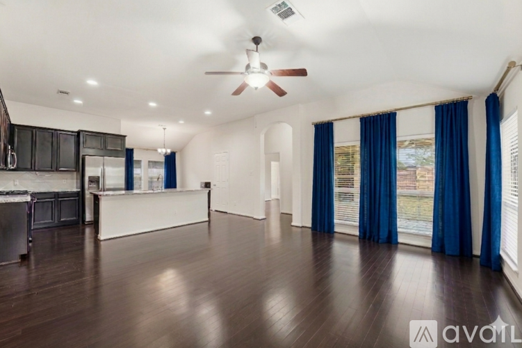 A spacious room with a ceiling fan and dark wood flooring.