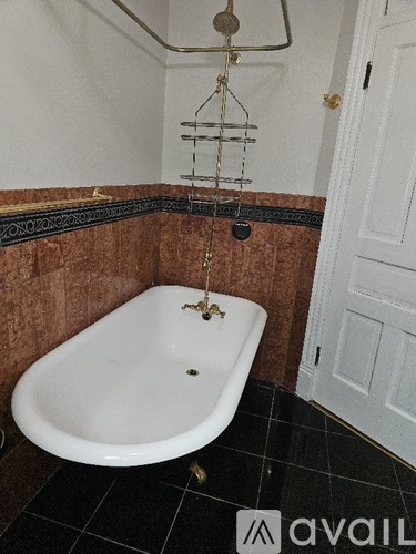 A white claw foot tub sits in a bathroom with a black tiled floor.