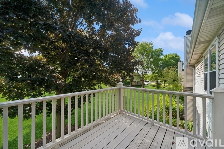 A wooden deck with a white railing overlooks a green lawn and trees.