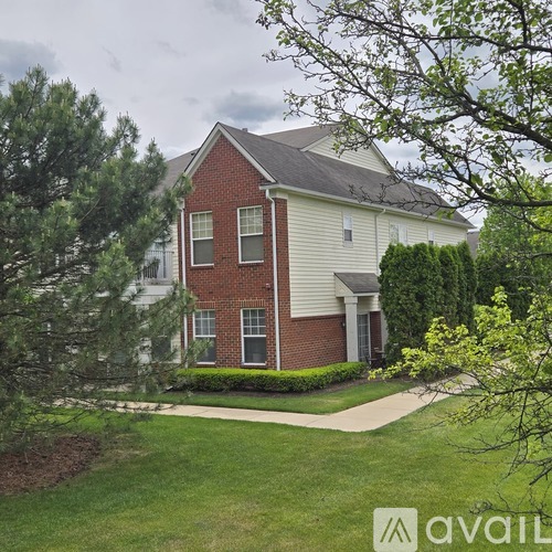 A house with a red brick facade and white siding is surrounded by a well-manicured lawn and trees.
