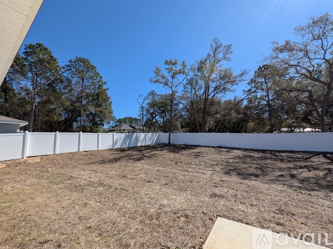 A white fence encloses a grassy area with trees in the background.
