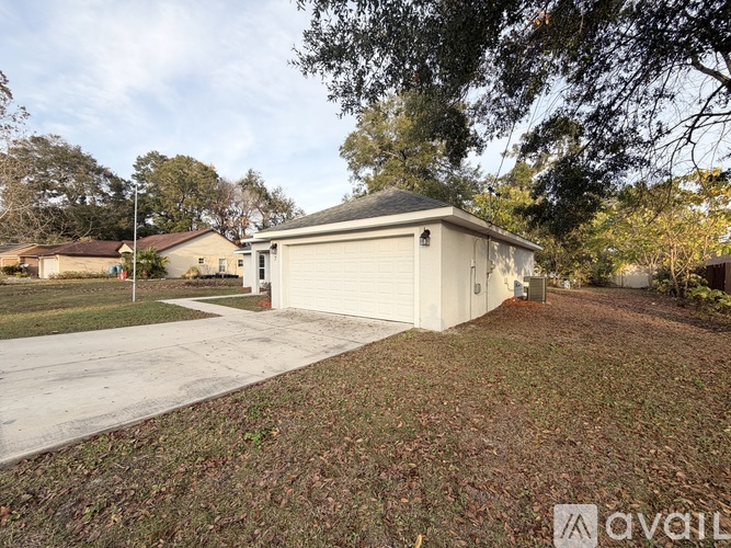 A detached house with a garage is surrounded by a grassy area and trees.
