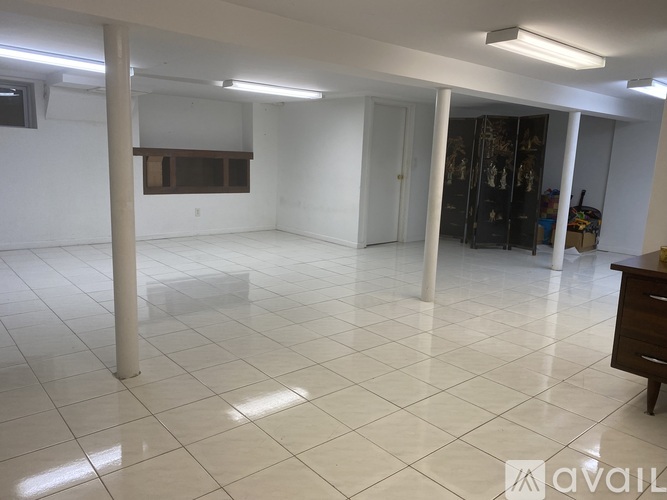 A spacious room with white tiled flooring and a cabinet in the corner.