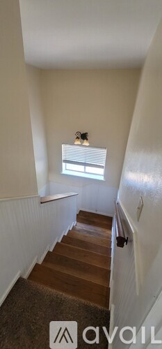 A staircase with a carpeted runner and wooden steps leading to a window with blinds.