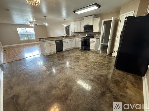 A kitchen with a black refrigerator and brown flooring.