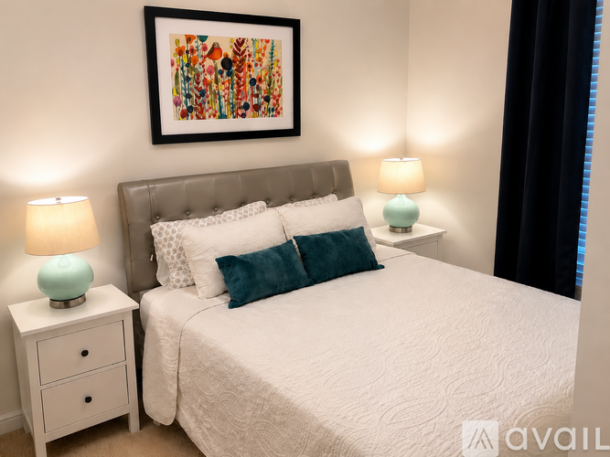 A bedroom with a large bed, two nightstands with lamps, and a colorful painting on the wall.
