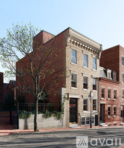 A street view of a red brick building with a tree in front.